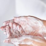 Woman washing her hands at the kitchen sink. There are vegetables out of focus in the background.